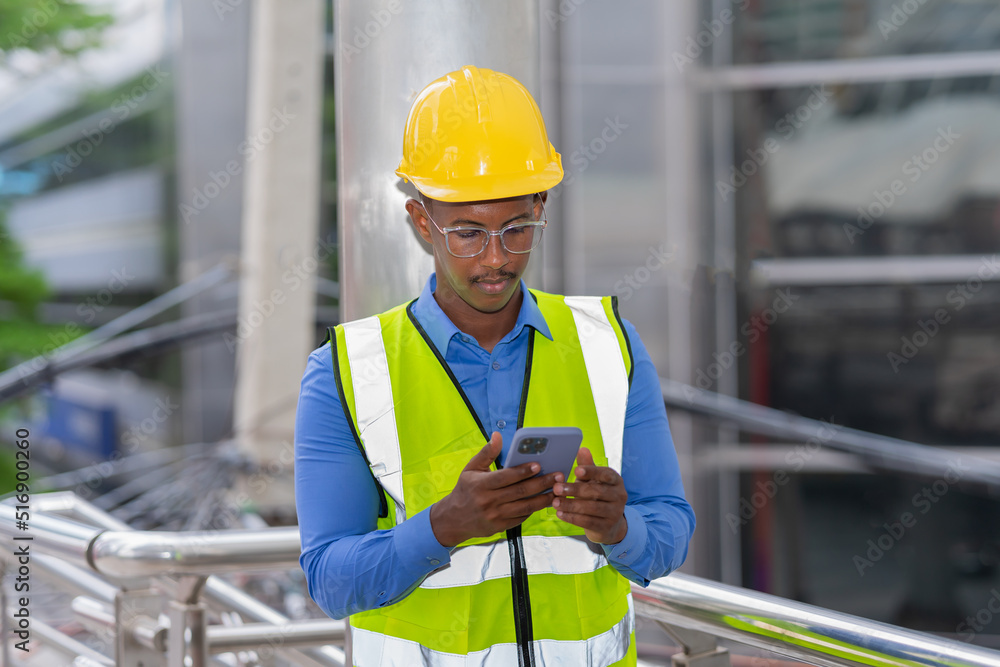 black engineer with glasses wear glow shirt and helmet, using mobile phone while working at construction site outside building in city black engineer with glasses wear glow shirt and helmet, using mobile phone while working at construction site outside building in city