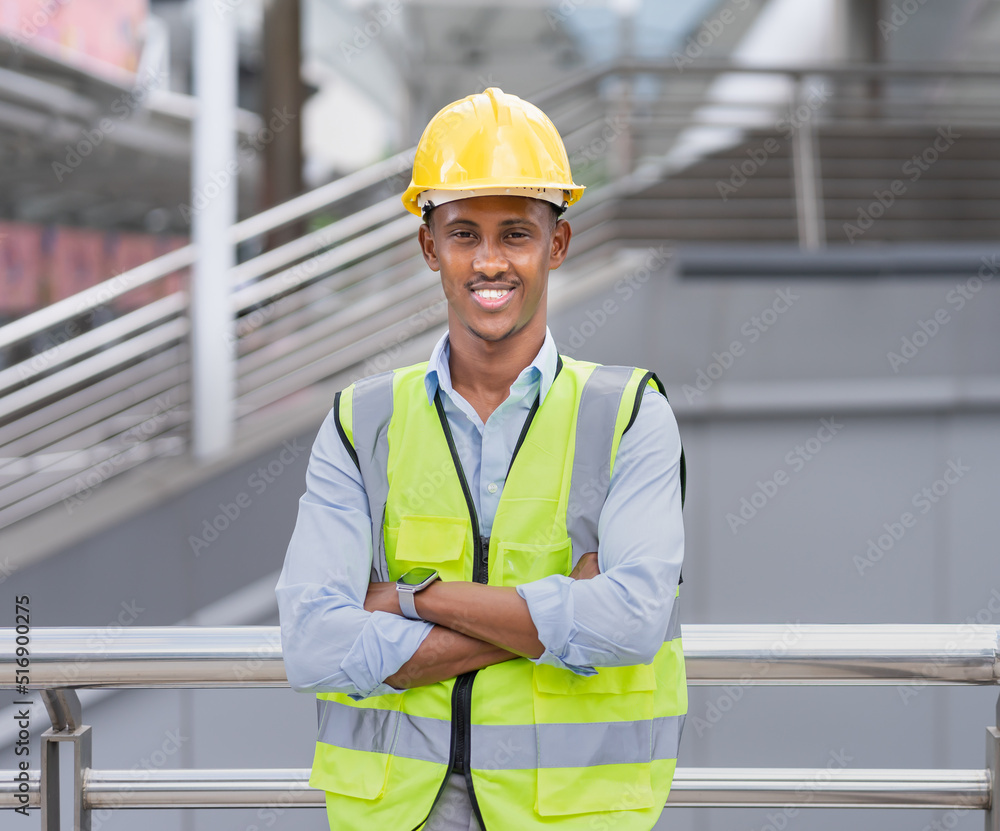 portrait of black engineer in glow shirt, smile, cross arm, wear helmet, looking at camera at construction site outside building in city portrait of black engineer in glow shirt, smile, cross arm, wear helmet, looking at camera at construction site outside building in city