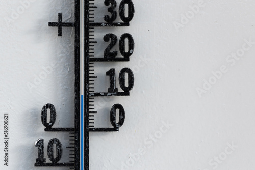 Classic black analog thermometer hanging on white wall displaying blue temperature scale of ten, 10 degrees celsius photo