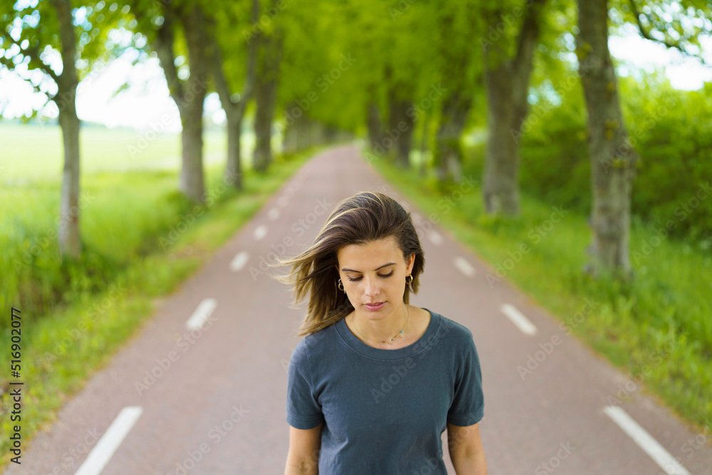 Young woman walking on road by trees Young woman walking on road by trees