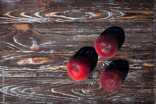 Still life of three ripe appetizing peaches, on a dark brown wooden textured table, for your design or illustrations.