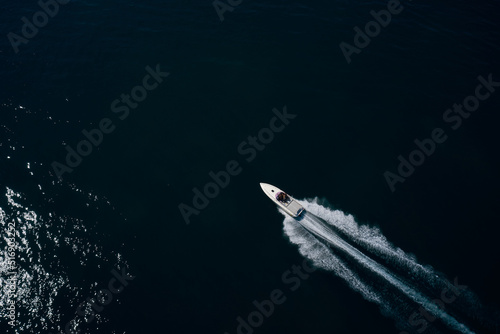 Speedy white boat movement on dark water aerial view. Expensive big super speed white boat with people moving on dark water top view. © Berg