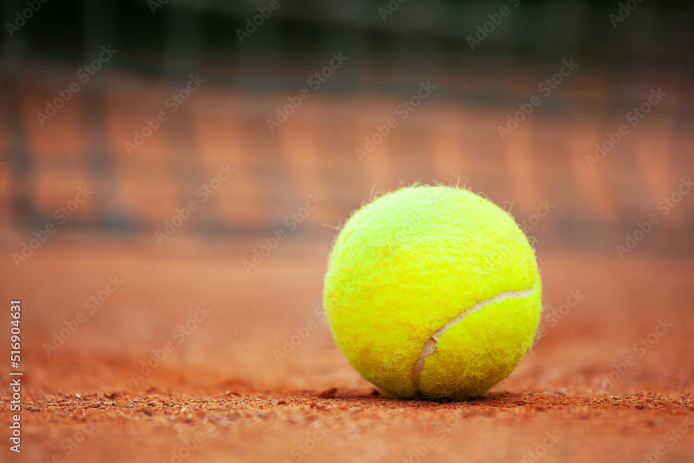 Yellow tennis ball lies on the clay court close up.