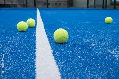 Selective focus. Blue paddle tennis court with synthetic grass and several yellow balls. Racket sports concept © Vic