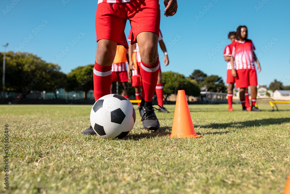 Low section of male multiracial players dribbling ball between cones at playground against clear sky Low section of male multiracial players dribbling ball between cones at playground against clear sky