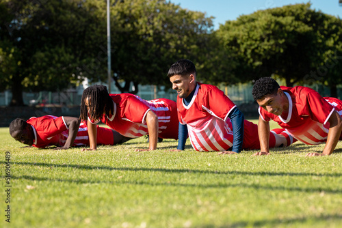 Male multiracial players wearing red uniforms doing push-ups on grassy playground in summer © WavebreakMediaMicro