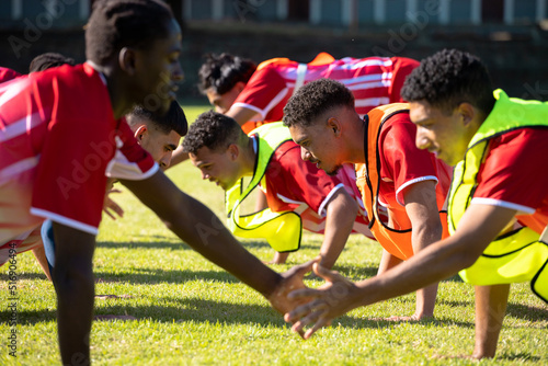 Male multiracial players in red uniforms practicing high five push-ups in a row on grassy field © WavebreakMediaMicro