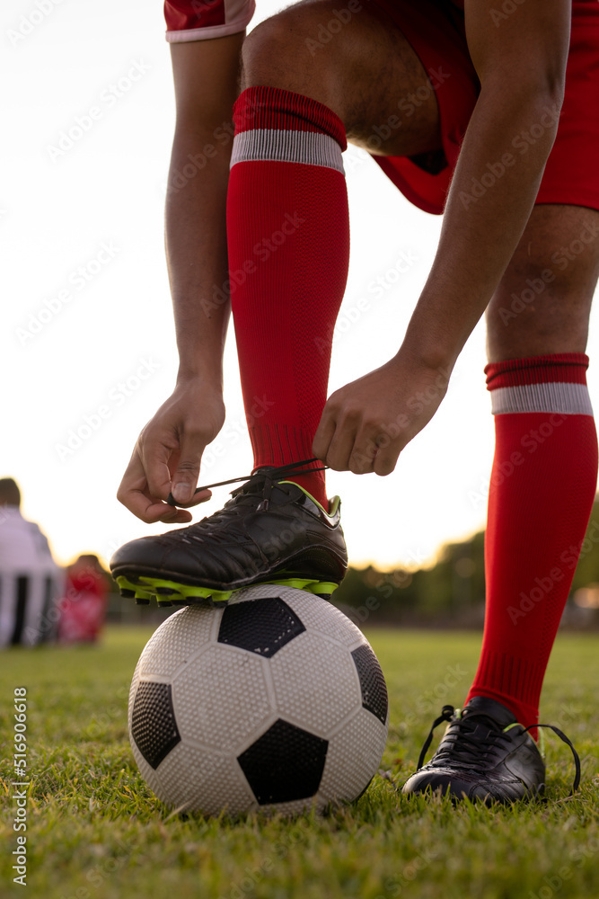 Low section of caucasian male athlete wearing red socks with leg on soccer ball tying shoelace Low section of caucasian male athlete wearing red socks with leg on soccer ball tying shoelace