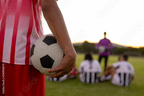 Midsection of caucasian male player in red jersey holding soccer ball standing against clear sky © WavebreakMediaMicro