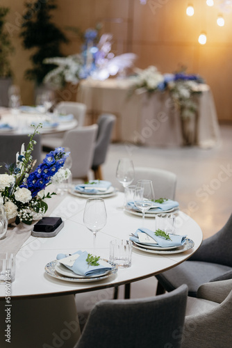 Wedding Decor. Festive table decorated with flowers on the center, candles, silverware and plates with silk napkins on dusty blue tablecloth