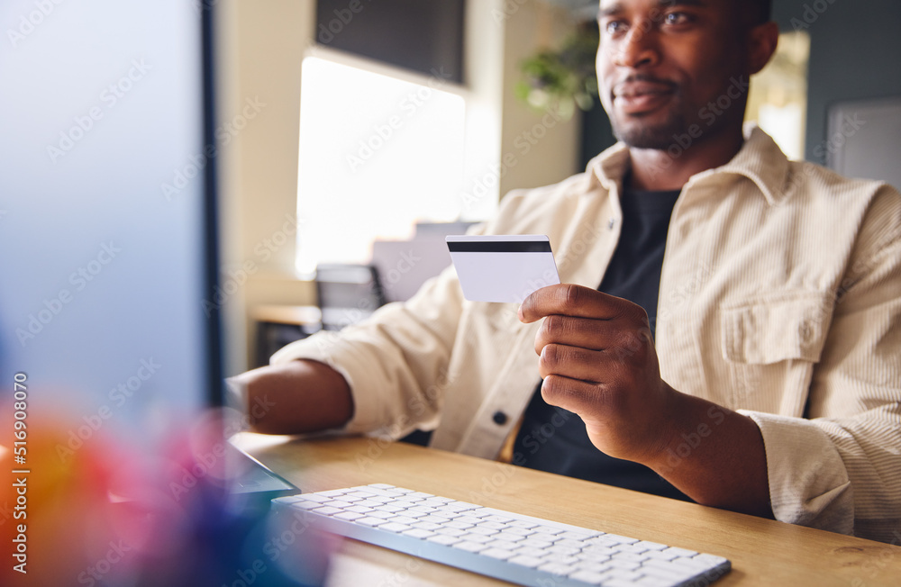 Fototapeta premium Man making online payment on computer holding credit card in office, business banking