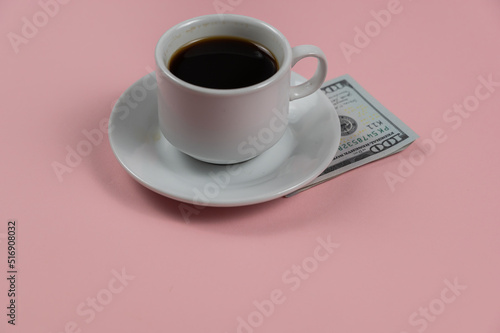 Espresso coffee and money against a pink background. A hundred-dollar bill lies under a white cup and saucer. A tip for the waiter. Close-up. Selective focus.