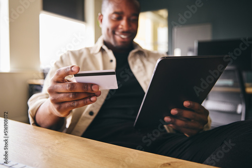 Smiling Man making online payment on tablet computer focused on credit card