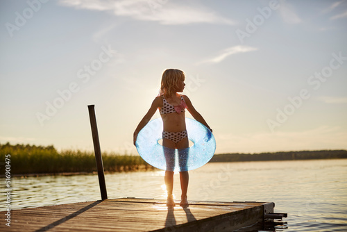 Girl in swimsuit with inflatable toy by lake at sunset