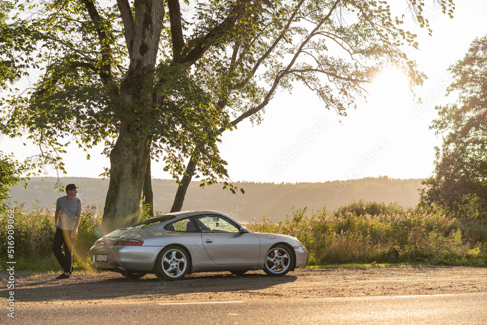 Man standing by sports car on rural road Man standing by sports car on rural road