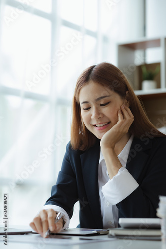 Asian woman looking at documents at a desk in a startup company, she is a financier overseeing the company's finances in accordance with policy and accuracy. Concept of corporate financial management.