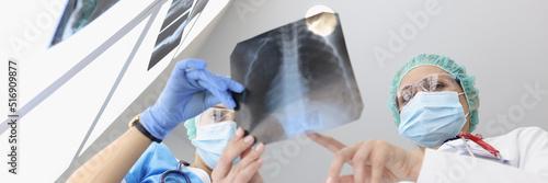 Doctors in medical gowns examine x ray of patient lungs in clinic