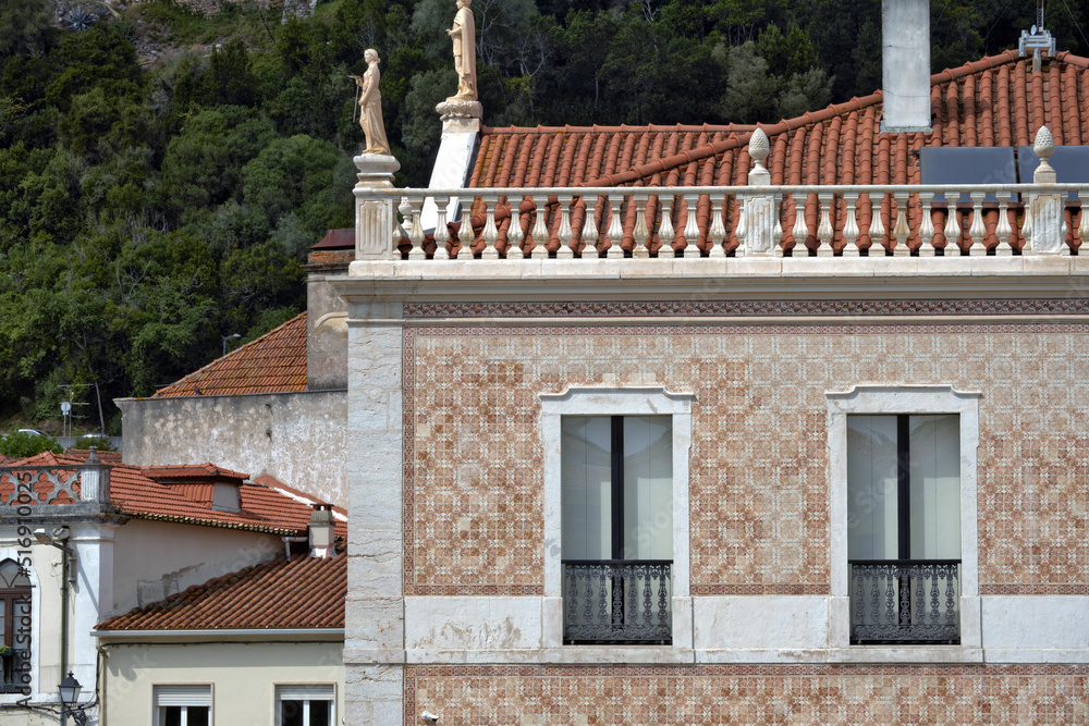Traditional statue as a decoration on the roof of a classic house and facade covered with azulejos in Leiria, Portugal