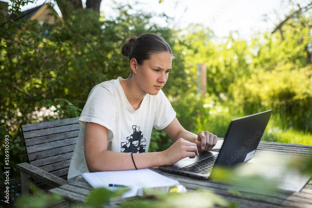 Teenage girl doing homework on laptop at outdoor table Teenage girl doing homework on laptop at outdoor table