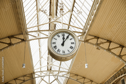 Round Roman clock at railway or subway station. Twelve o'clock, five past twelve pm, close-up