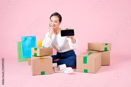 Satisfied woman sitting on floor, showing cell phone with blank black screen for promotion of delivery service.