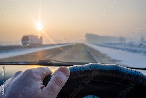 view of the driver hand on the steering wheel of the car while driving on a slippery snow covered road