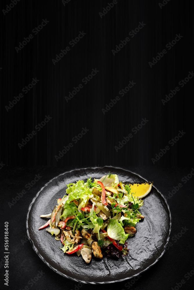 Salad with mussels, on a black plate. vertical Salad with mussels, on a black plate. vertical