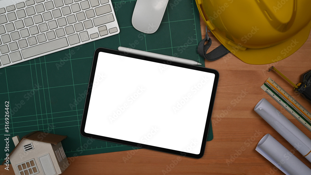 Naklejka premium Digital tablet, protective helmet and blueprints on a wooden table. Engineer, Architect office desk