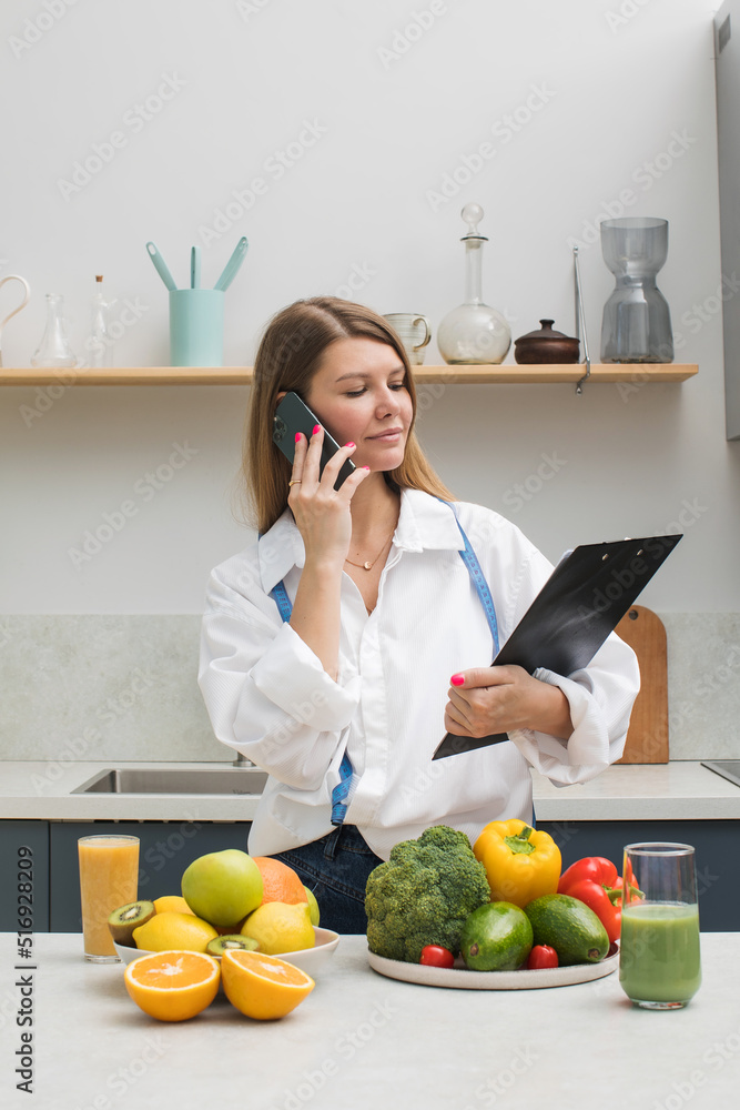 Confident nutritionist with clipboard talks via smartphone at table with fruits