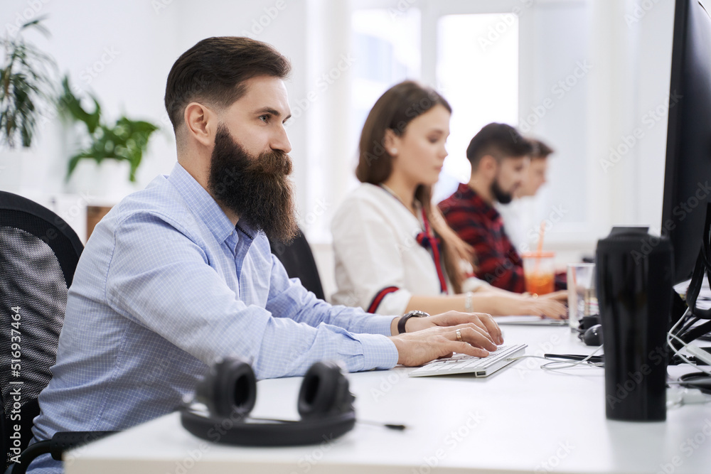People working in modern IT office. Group of young and experienced programmers and software developers sitting at desks working on computers. Team at work.