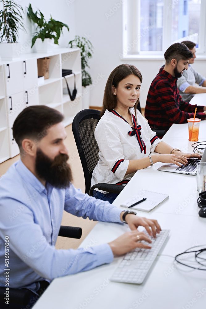 People working in modern IT office. Group of young and experienced programmers and software developers sitting at desks working on computers. Team at work.