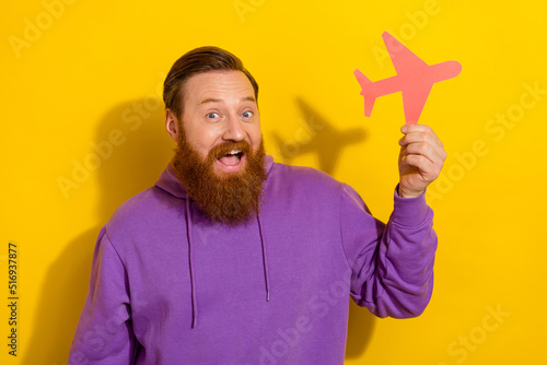 Portrait of young overjoyed cheerful male hold plane card go on trip visit many countries isolated on yellow color background