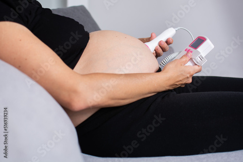 Fototapeta Pregnant woman with a fetal doppler listening to the baby's heart sitting on the