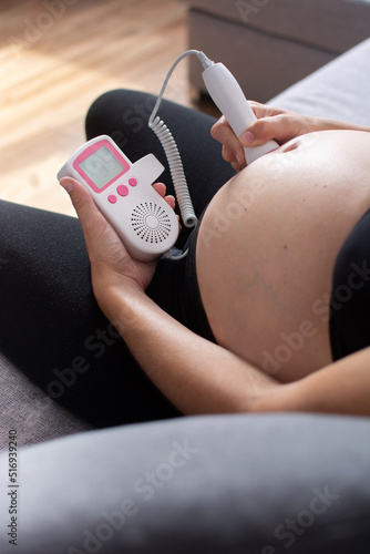 Photo Pregnant woman with a fetal doppler listening to the baby's heart sitting on the