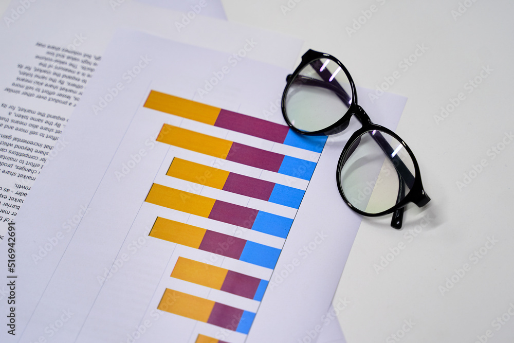 Stylish eyeglasses and colorful chart on the white work table. Business concept.