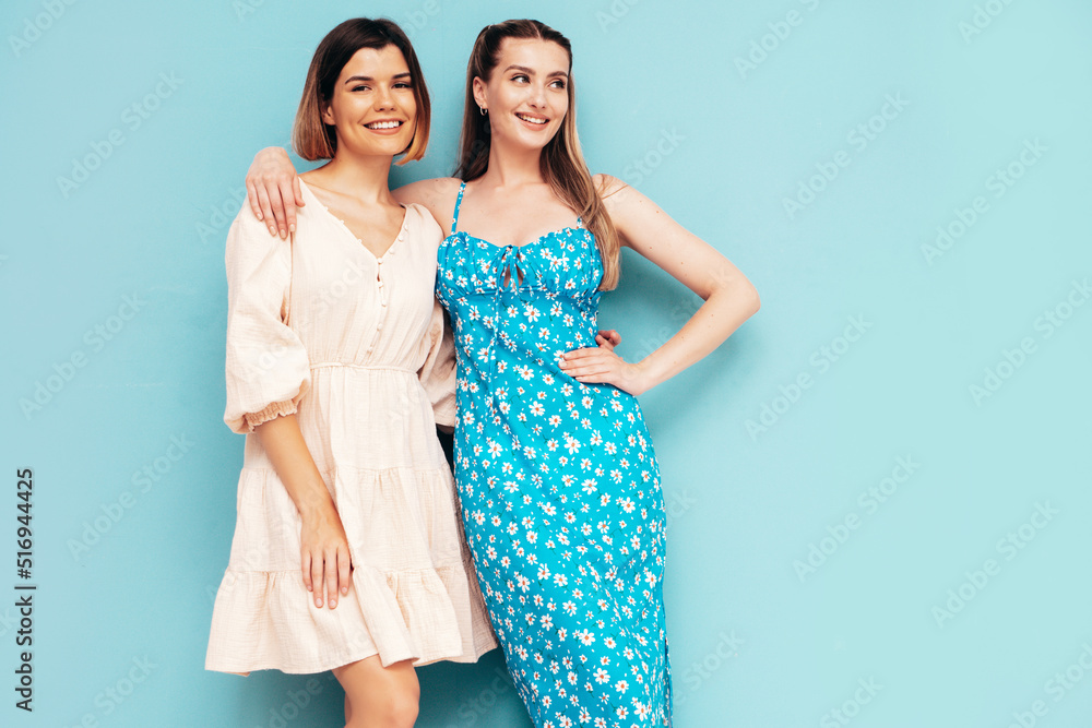 Two young beautiful smiling brunette hipster female in trendy summer dresses. Sexy carefree women posing near blue wall. Positive models having fun. Cheerful and happy. Isolated Two young beautiful smiling brunette hipster female in trendy summer dresses. Sexy carefree women posing near blue wall. Positive models having fun. Cheerful and happy. Isolated