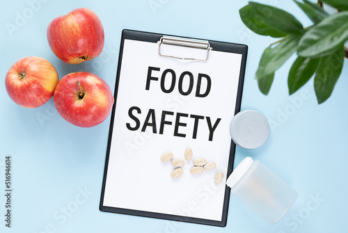Fototapeta Naklejka Na Ścianę i Meble -  Food safety text on a paper tablet with pills lying on a blue table with apples. Can be used as concept photo