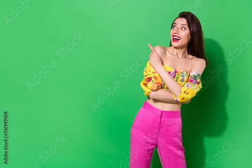 Portrait of excited cheerful girl look direct finger empty space offer proposition isolated on green color background
