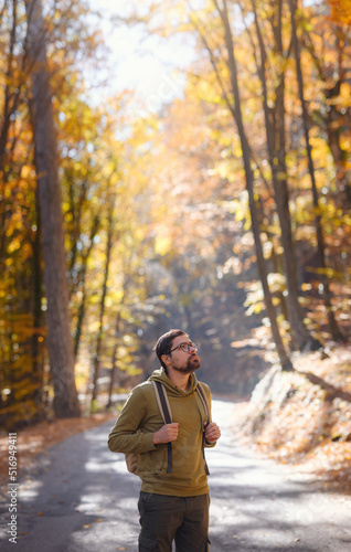 Young handsome man posing in autumn forest. young hipster guy with backpack , traveller standing in woods, Hiking, Forest, Journey, active healthy lifestyle, adventure, vacation concept. © YURII Seleznov