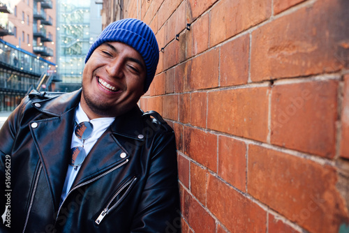 Photography Latin Man with perfect teeth smiling standing next to the red brick wall