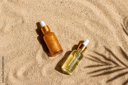 Liquid cosmetic product in glass bottle on sandy beach and palm leaf shadow. Hyaluronic acid and shine oil cosmetic mock up. Summer skin care concept, top view, flat lay image.