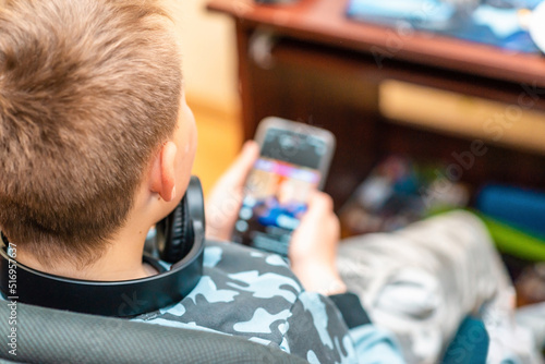 A boy 10s watches a video clip in a smartphone at home. Back view,closeup.Selective focus.