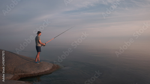 A man with a fishing rod in the process of fishing on the shore of a calm sea