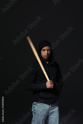 African american hooligan holding baseball bat and looking at camera isolated on black