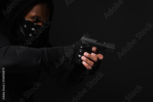African american bandit with obscure face holding handgun isolated on black