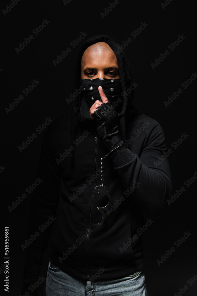 African american bandist in mask on face and handcuffs showing secret gesture isolated on black