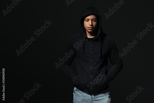 African american hooligan holding hands in pockets of hoodie isolated on black