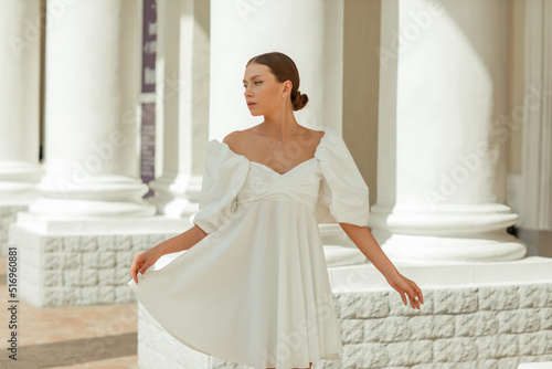 A young beautiful woman in a white dress near the columns