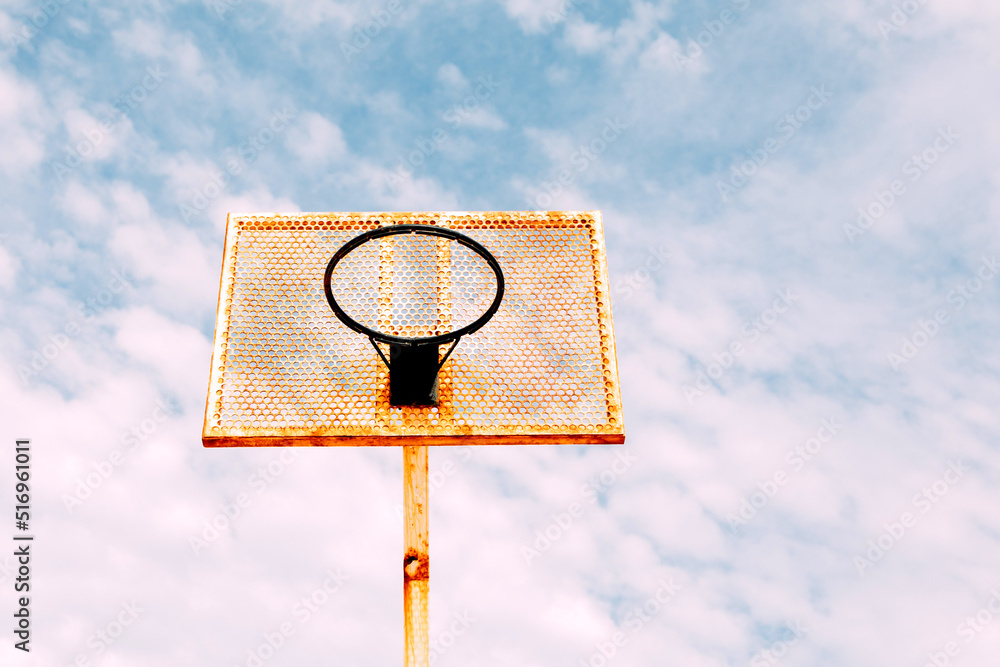 Botton view of basketball backboard under blue sky with clouds. Close up orange and rusty metal basketball backboard. No people