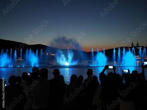 Silhouette of people watching at colorful illuminated musical fountains in the evening. Light and water night show performance.